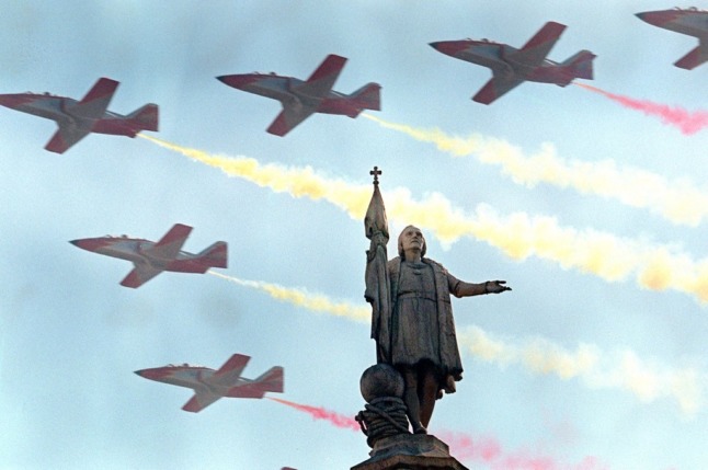 Military jets create a Spanish flag in the sky over Madrid, with a statue of Cristopher Columbus in the foreground. Photo: DOMINIQUE FAGET / AFP)
