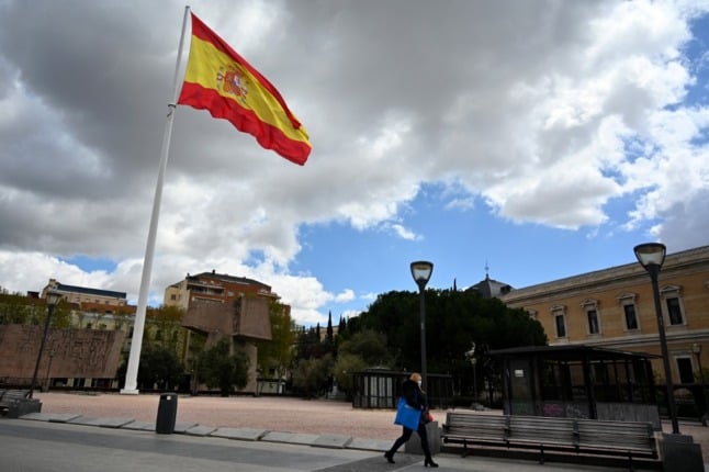 A Spanish flag flutters as a woman wearing a face mask walks in Madrid on April 2, 2020 amid a national lockdown to fight the spread of the COVID-19 coronavirus. - The coronavirus death toll in Spain surged past 10,000 after a record 950 deaths in 24 hours, with the number of confirmed cases passing the 110,000 mark, the government said. (Photo by Gabriel BOUYS / AFP)