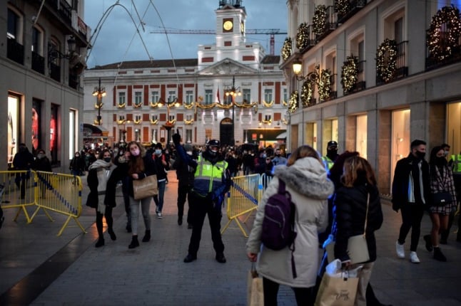 Spanish police officers stand guard as people shop for Christmas in the centre of Madrid on December 7, 2020.