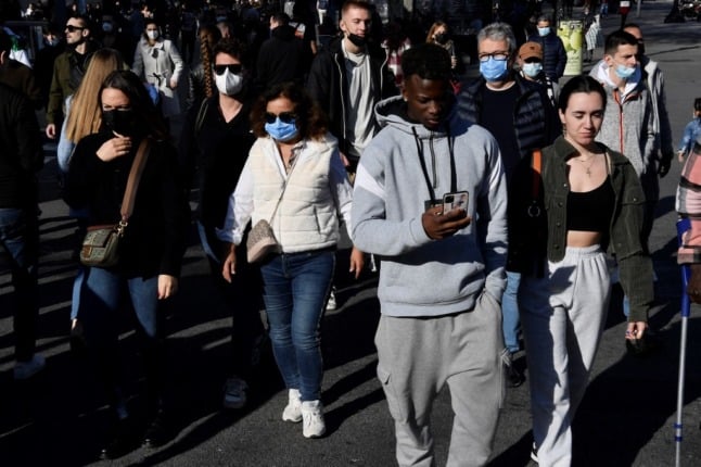 People, some wearing face-masks, walk in a street as they enjoy a day out in Barcelona on December 31, 2021. (Photo by Pau BARRENA / AFP)